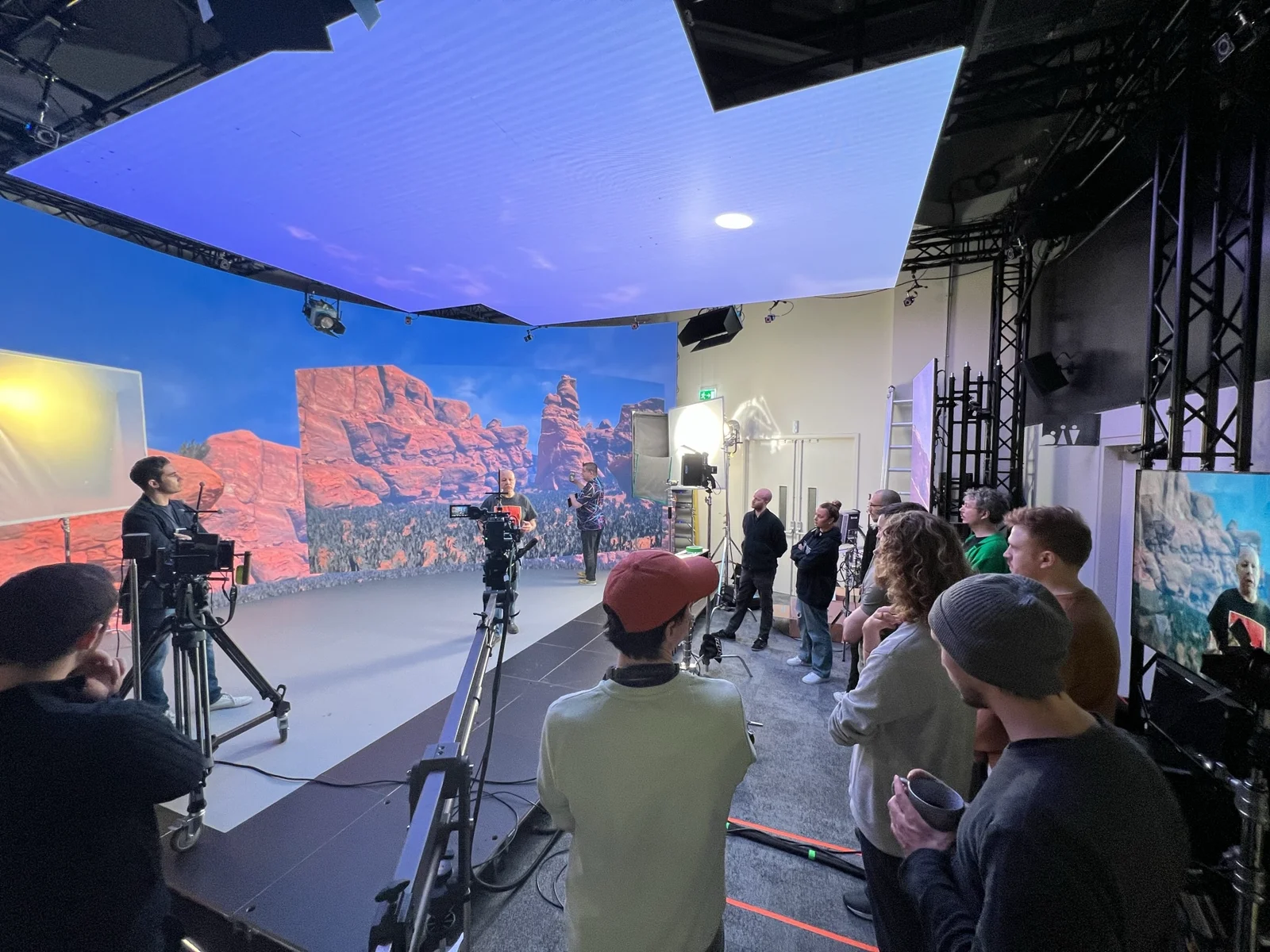A virtual production demonstration with cameras, an LED volume displaying a canyon, and a group watching